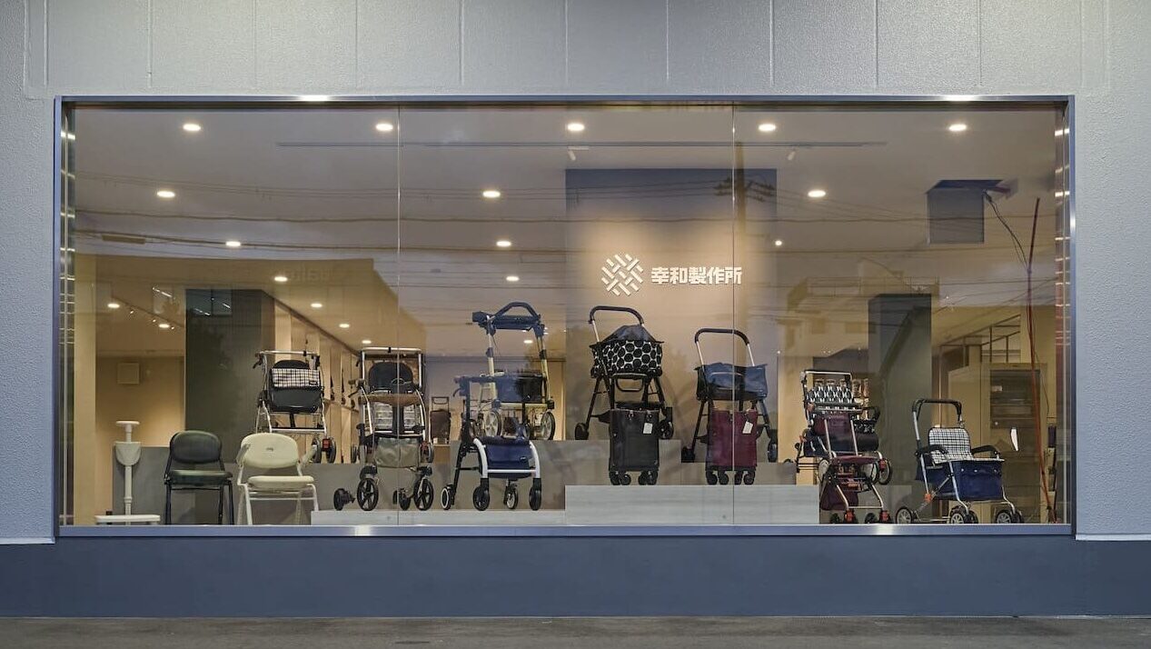 幸和製作所本社の外観。ガラス越しにシルバーカーや歩行補助器が展示されたショールームが見える建物。